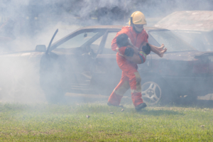 firefighter carrying person out of burning car
